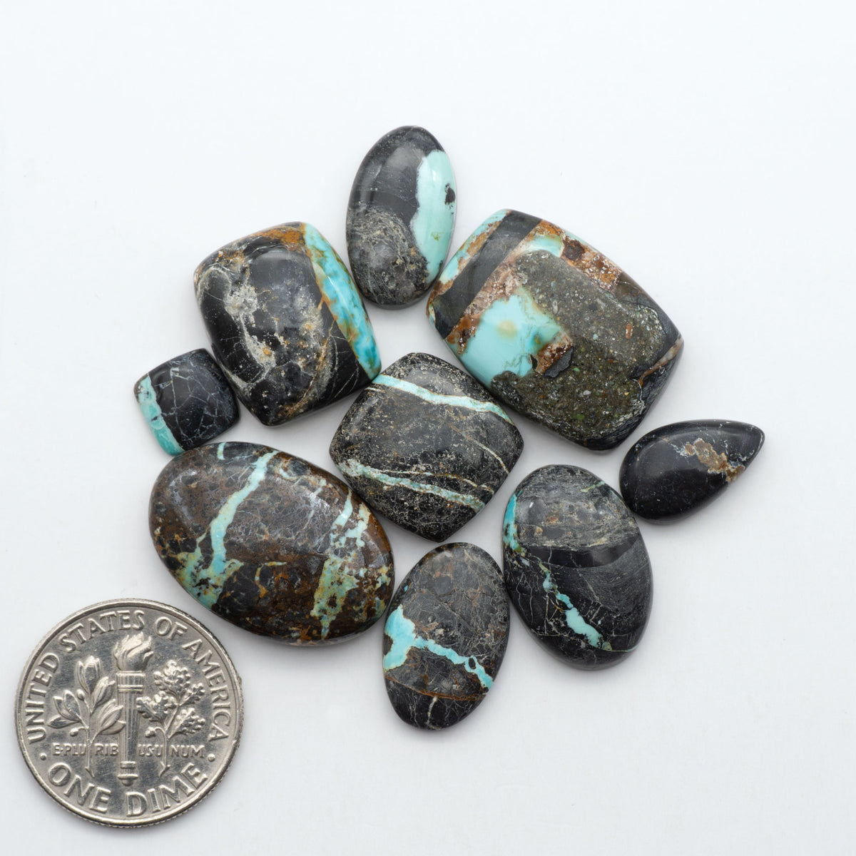 Black Jack turquoise cabochons, blue-green color with black matrix, polished stones on a white background with a US dime for scale