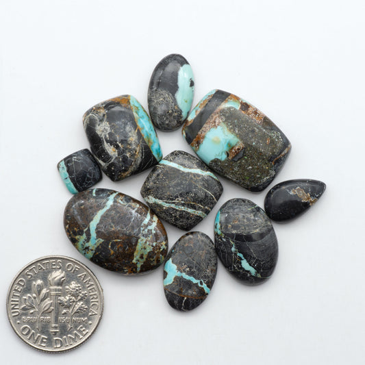 Black Jack turquoise cabochons, blue-green color with black matrix, polished stones on a white background with a US dime for scale