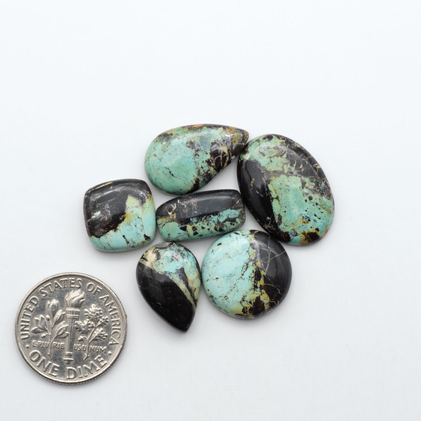 Black Jack turquoise cabochons, blue-green color with black matrix, polished stones on a white background with a US dime for scale