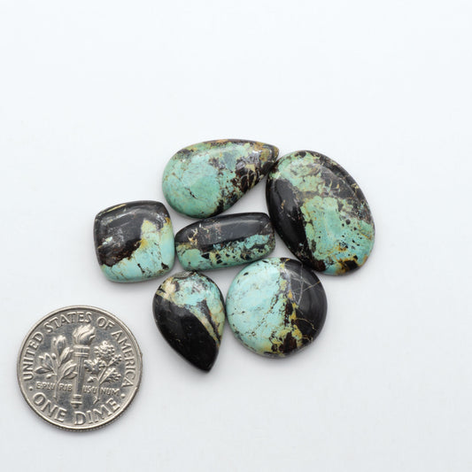Black Jack turquoise cabochons, blue-green color with black matrix, polished stones on a white background with a US dime for scale