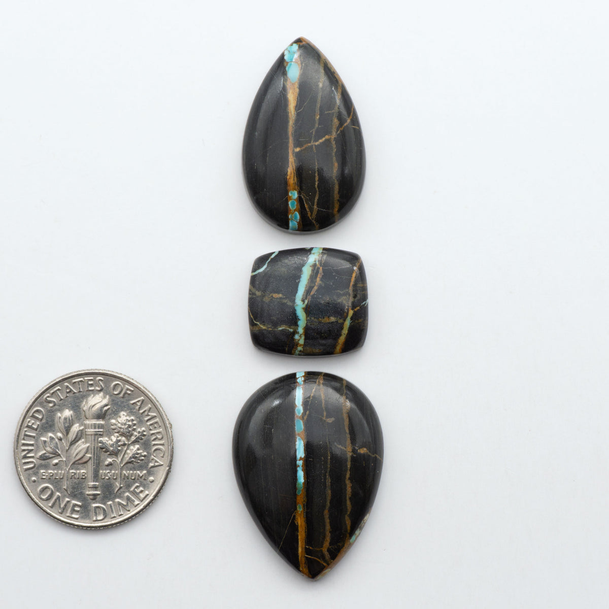 Black Jack turquoise cabochons, blue-green color with black matrix, polished stones on a white background with a US dime for scale