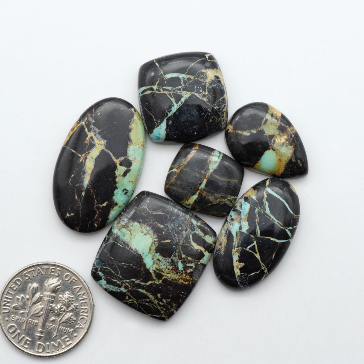 Black Jack turquoise cabochons, blue-green color with black matrix, polished stones on a white background with a US dime for scale