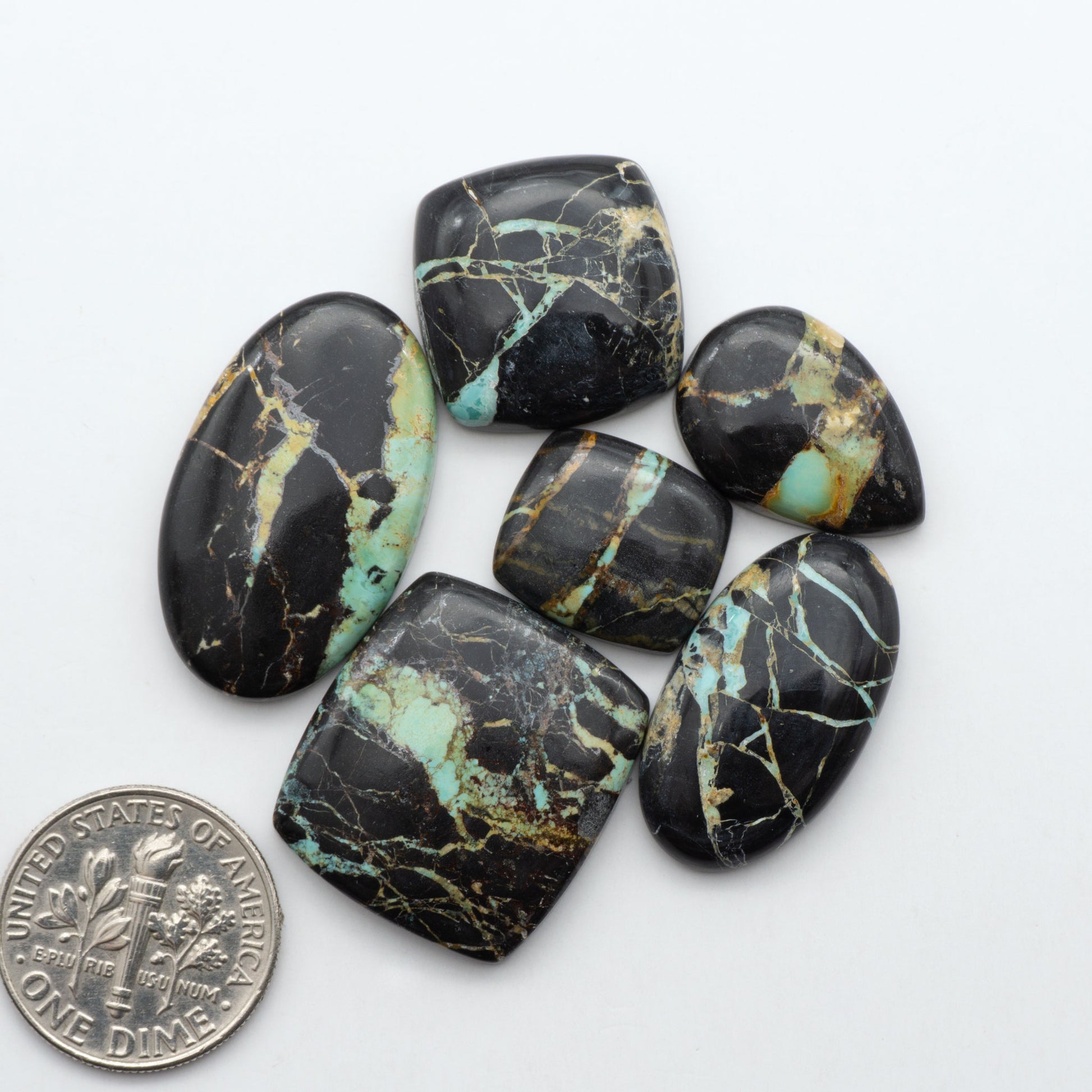 Black Jack turquoise cabochons, blue-green color with black matrix, polished stones on a white background with a US dime for scale