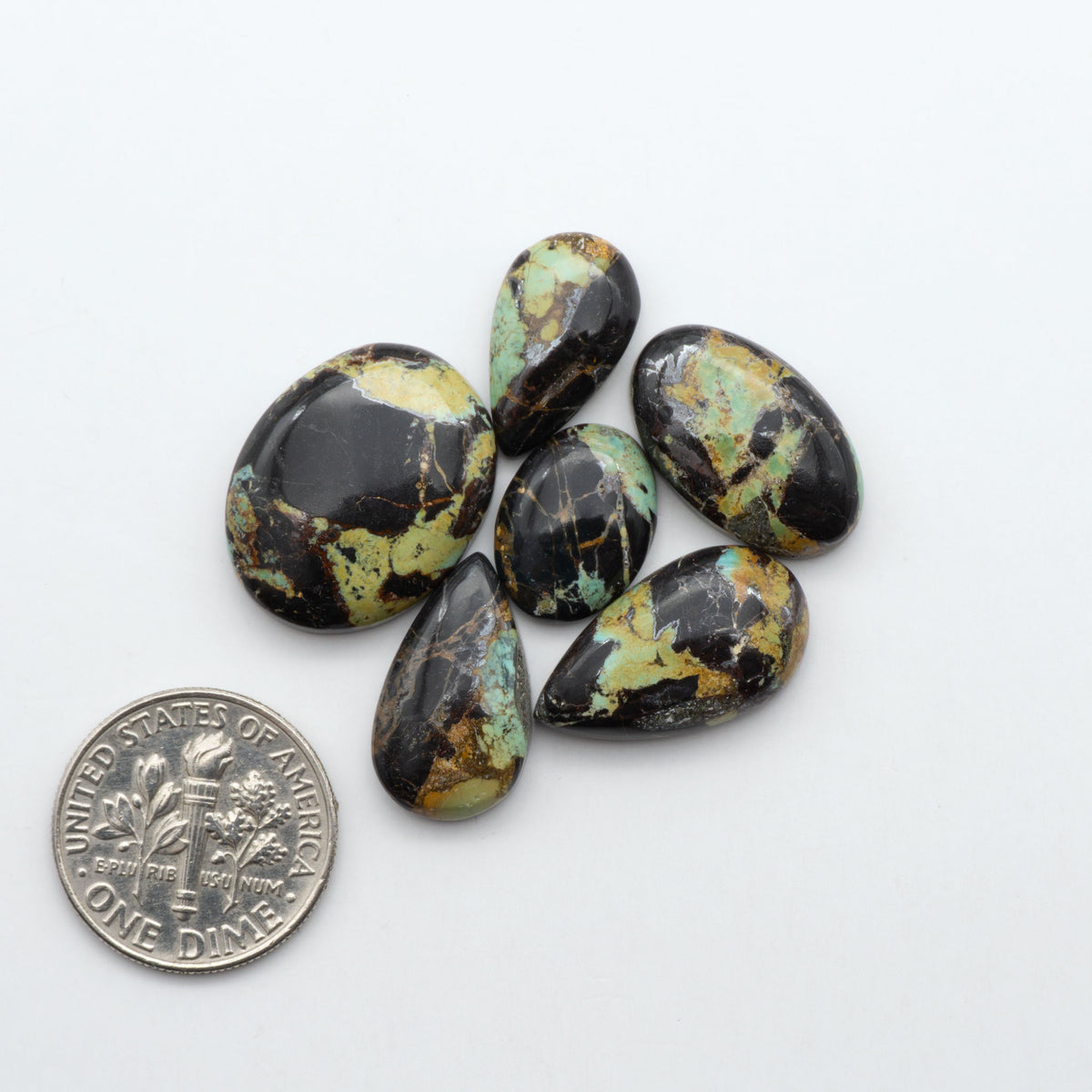 Black Jack turquoise cabochons, blue-green color with black matrix, polished stones on a white background with a US dime for scale