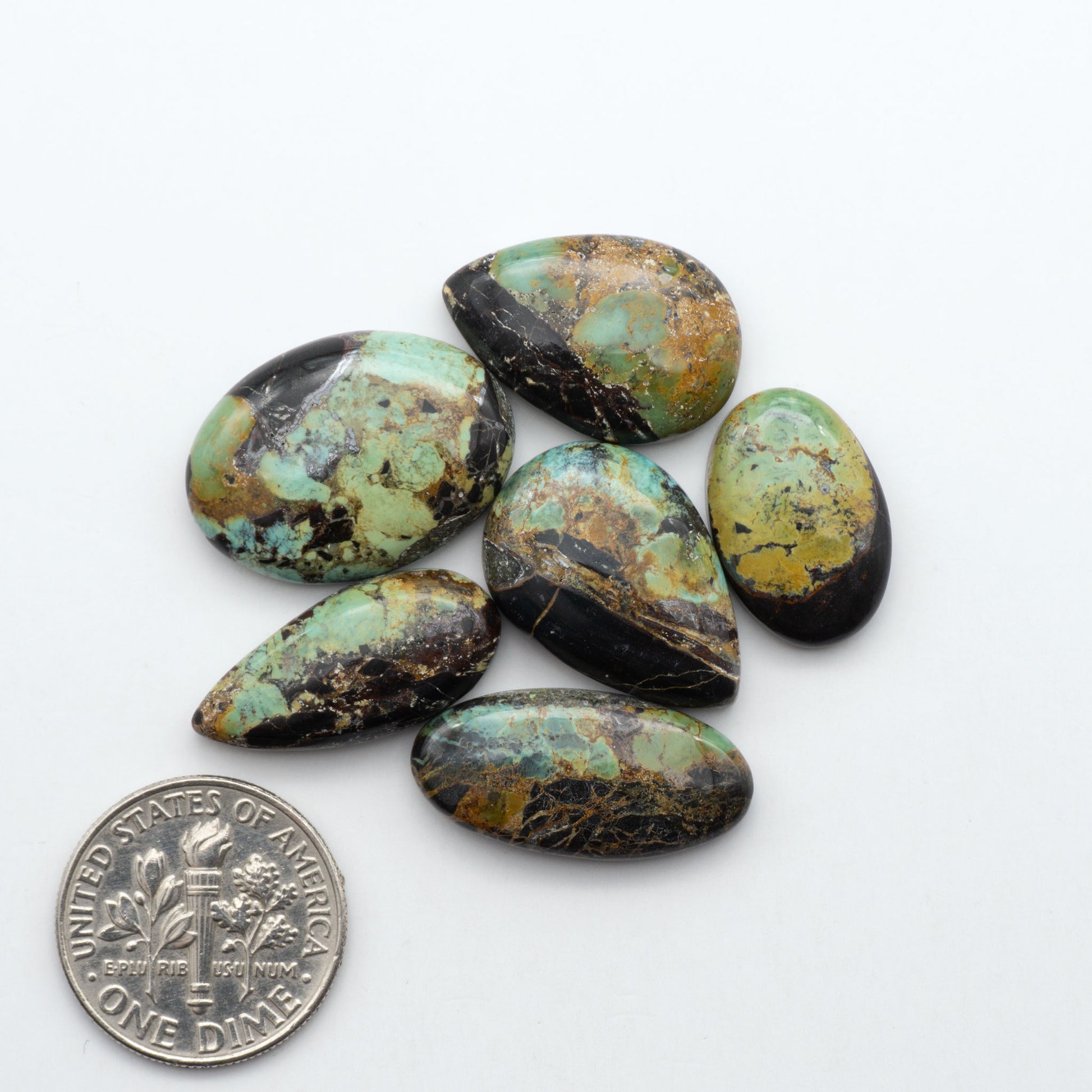Black Jack turquoise cabochons, blue-green color with black matrix, polished stones on a white background with a US dime for scale