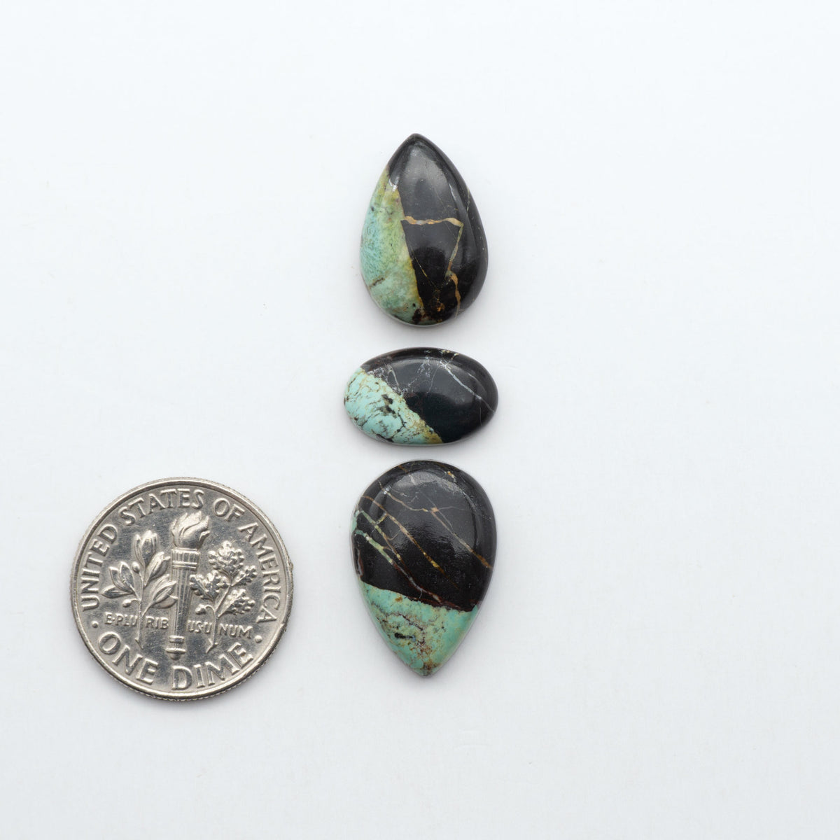 Black Jack turquoise cabochons, blue-green color with black matrix, polished stones on a white background with a US dime for scale