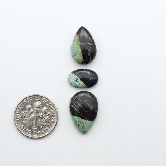 Black Jack turquoise cabochons, blue-green color with black matrix, polished stones on a white background with a US dime for scale