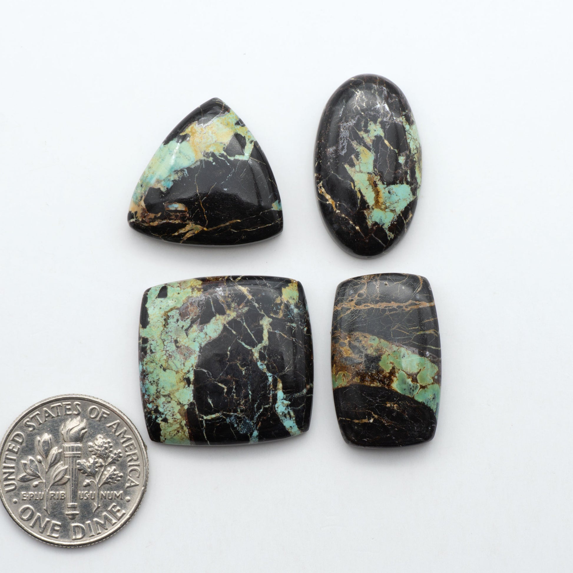 Black Jack turquoise cabochons, blue-green color with black matrix, polished stones on a white background with a US dime for scale