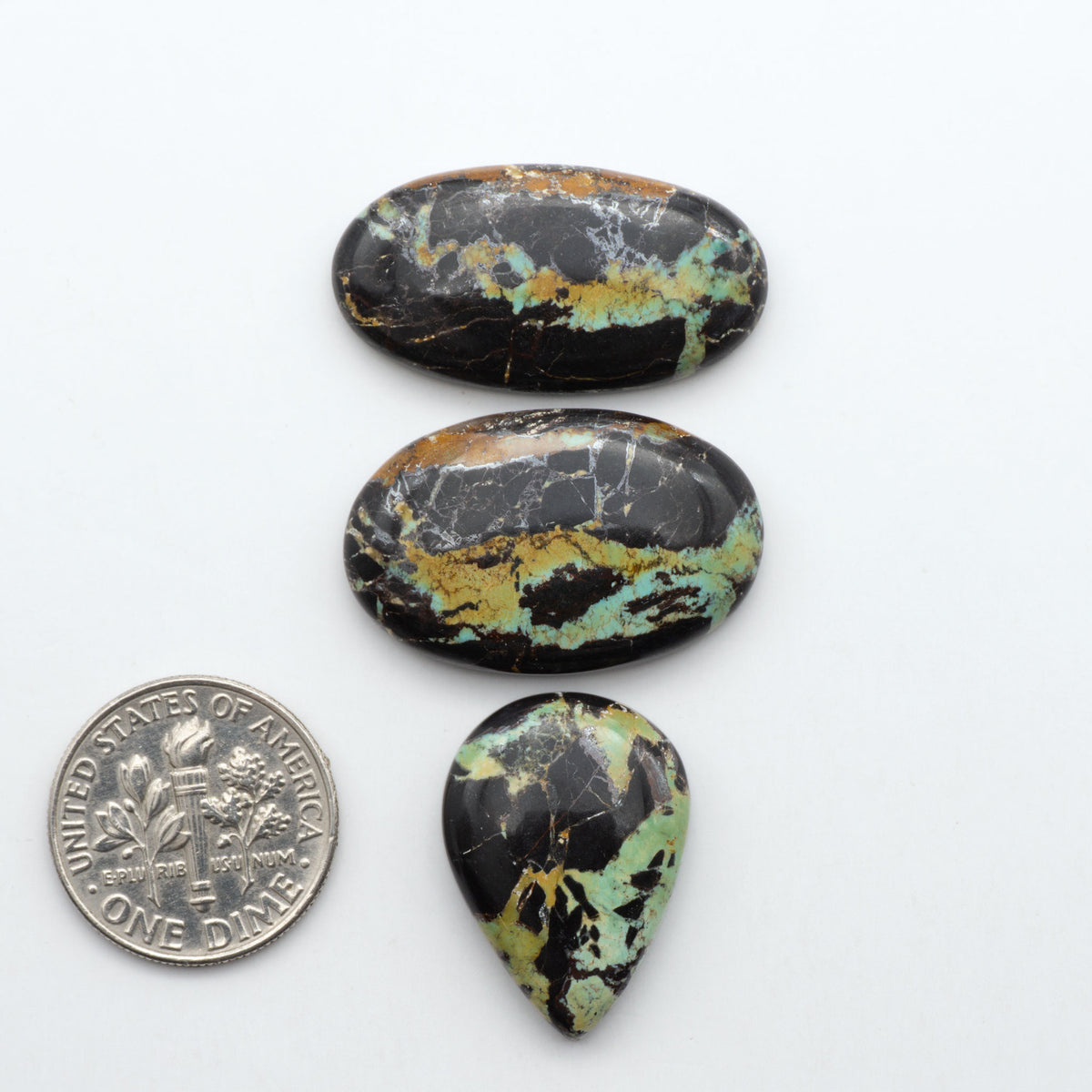 Black Jack turquoise cabochons, blue-green color with black matrix, polished stones on a white background with a US dime for scale