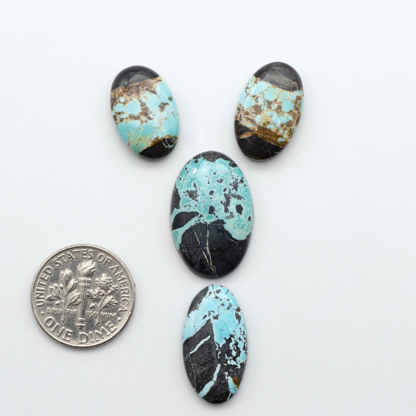 Black Jack turquoise cabochons, blue-green color with black matrix, polished stones on a white background with a US dime for scale