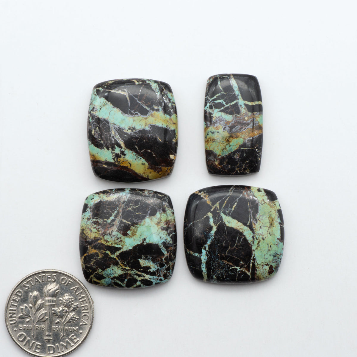 Black Jack turquoise cabochons, blue-green color with black matrix, polished stones on a white background with a US dime for scale