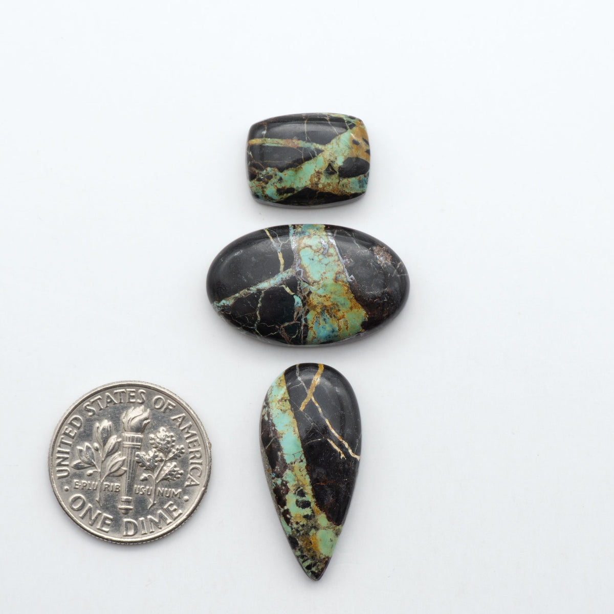 Black Jack turquoise cabochons, blue-green color with black matrix, polished stones on a white background with a US dime for scale