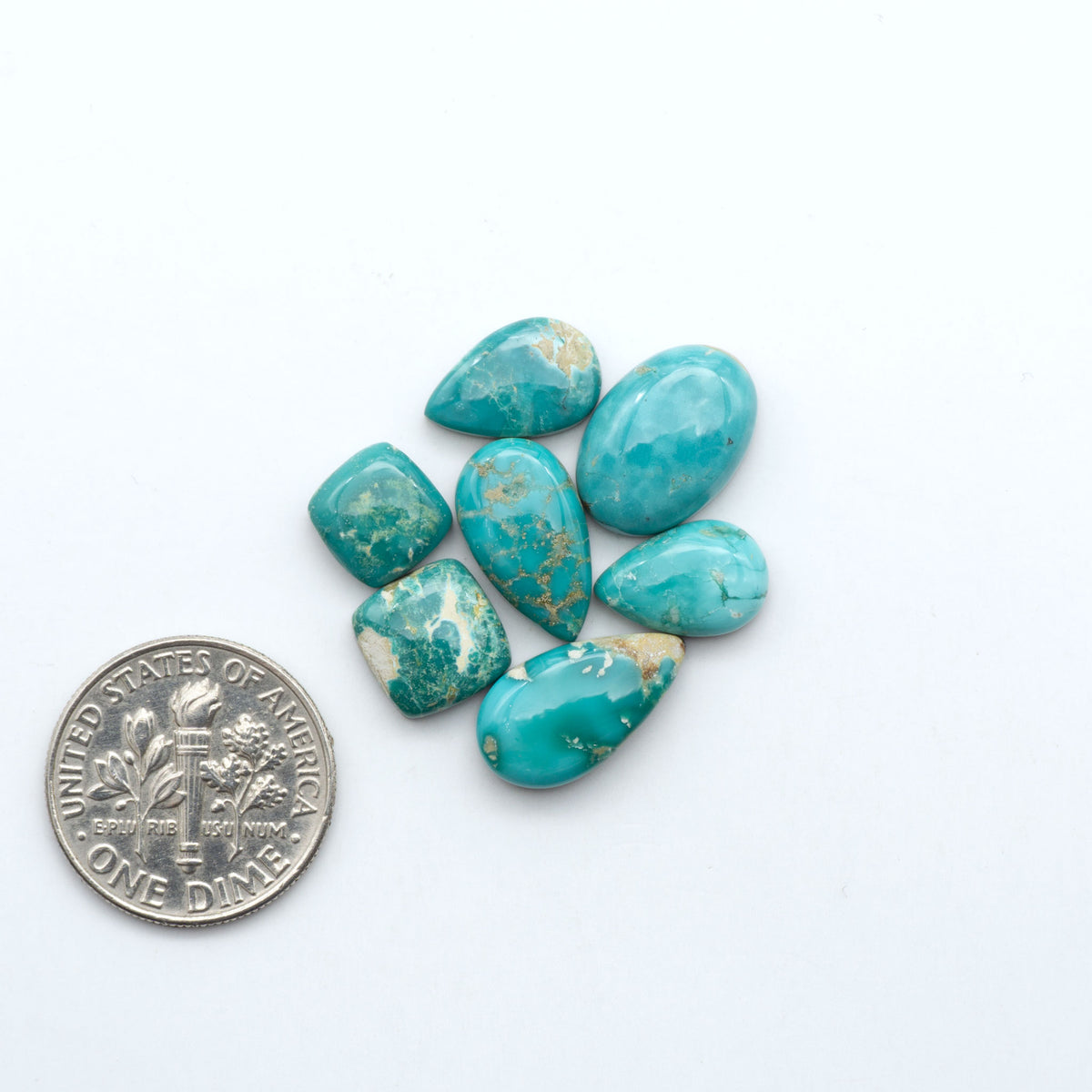 Fox Turquoise cabochons, polished gemstones with natural matrix on a white background, with a US dime for scale