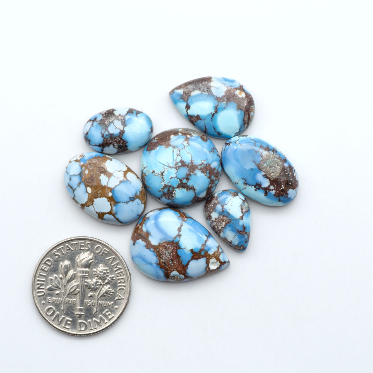 Golden Hills Turquoise cabochons, icy blue to lavender tones with chocolate matrix, polished stones on a white background with a US dime for scale