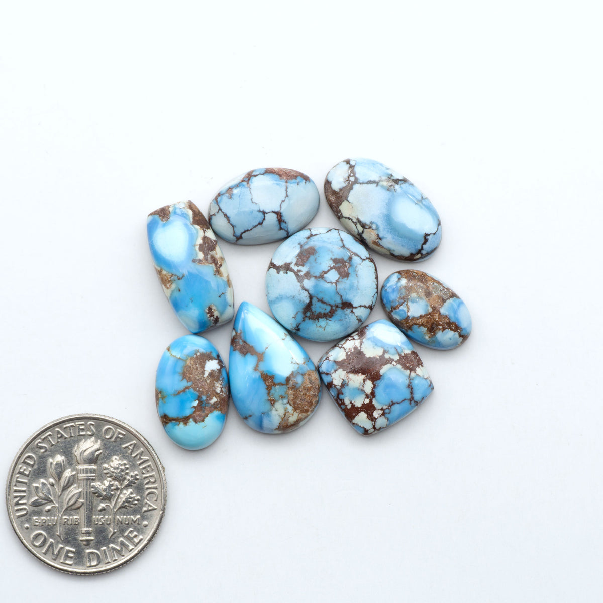 Golden Hills Turquoise cabochons, icy blue to lavender tones with chocolate matrix, polished stones on a white background with a US dime for scale