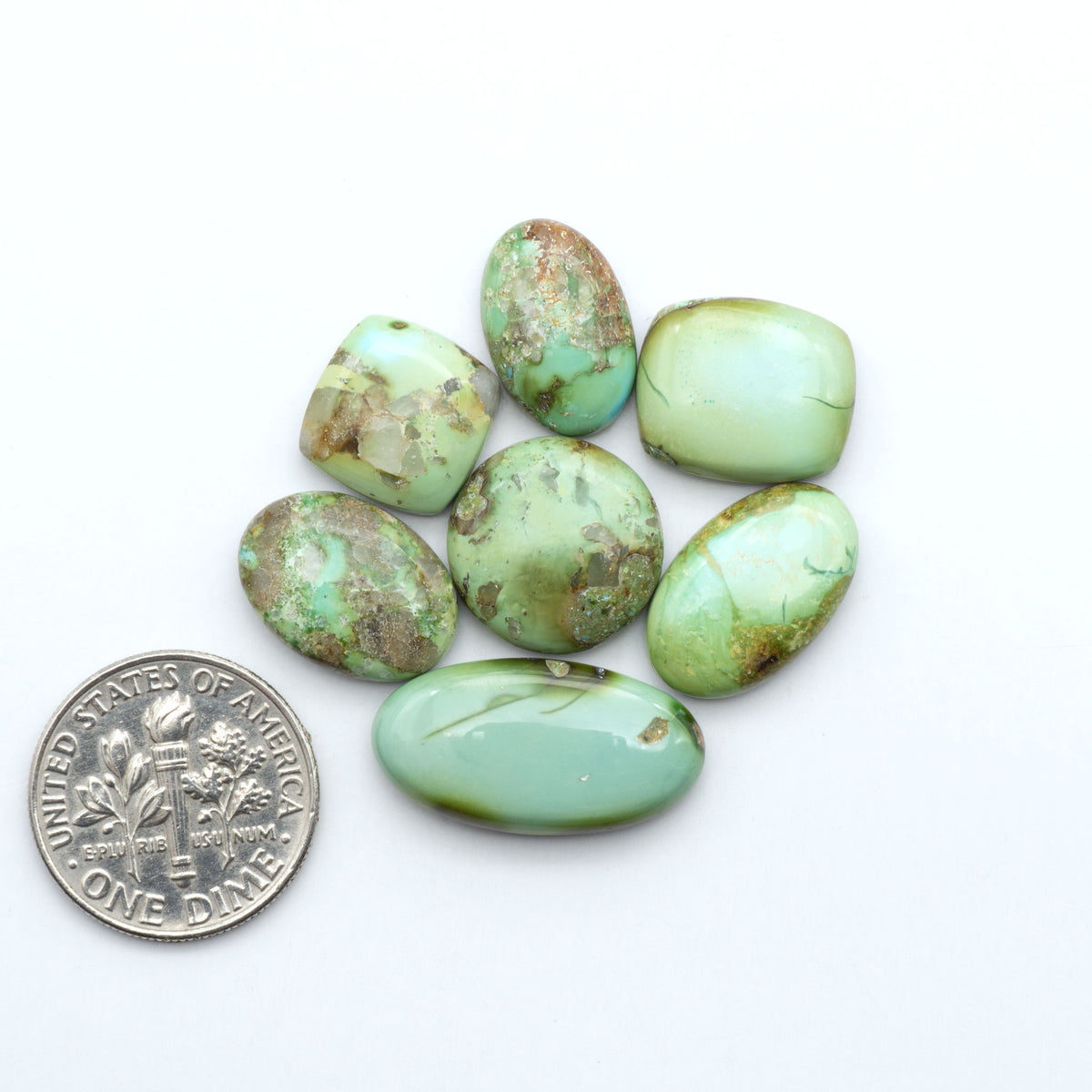 Sonoran Mountain Turquoise cabochons, blue-green color with natural matrix, polished stones on a white background, with a US dime for scale