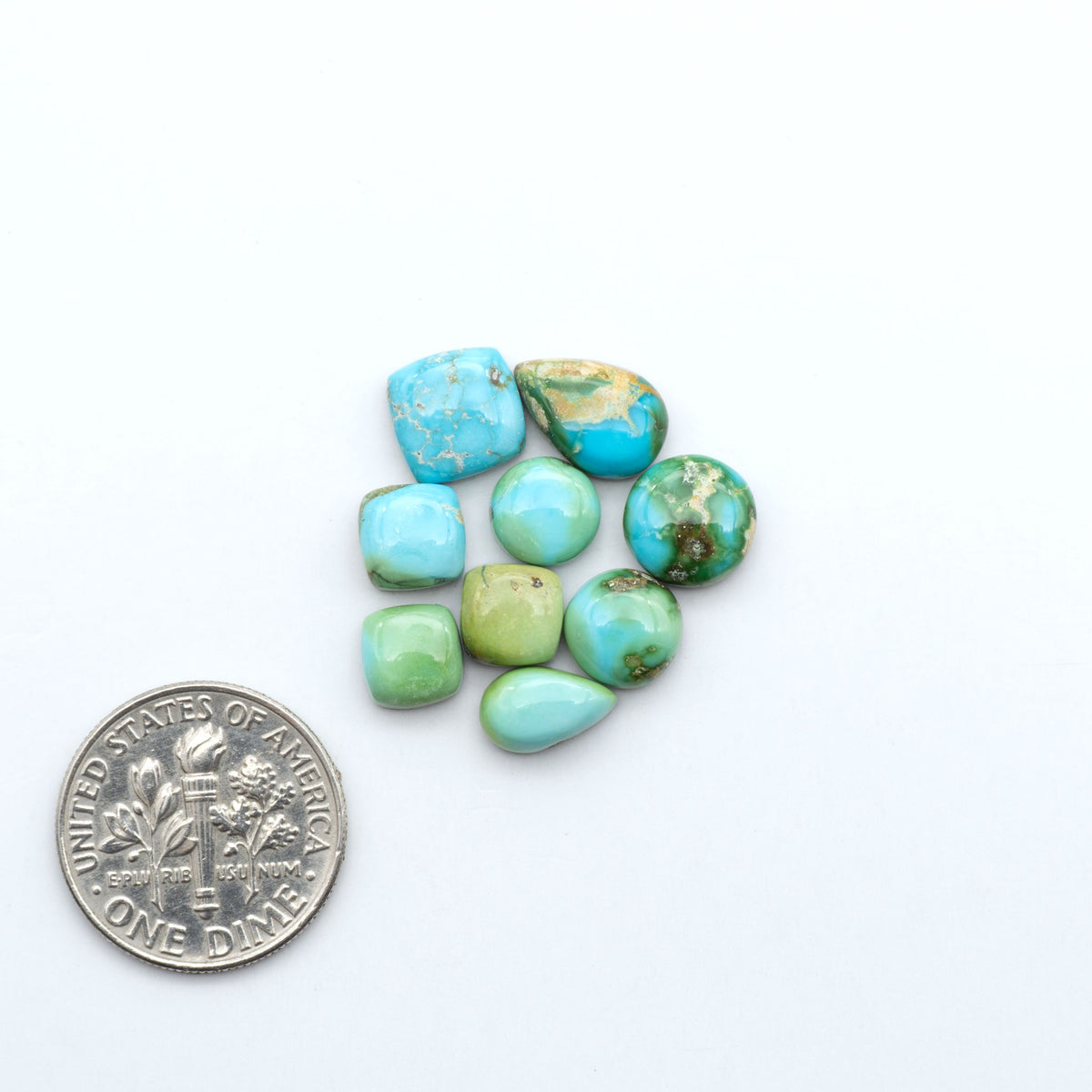 Sonoran Mountain Turquoise cabochons, blue-green color with natural matrix, polished stones on a white background, with a US dime for scale
