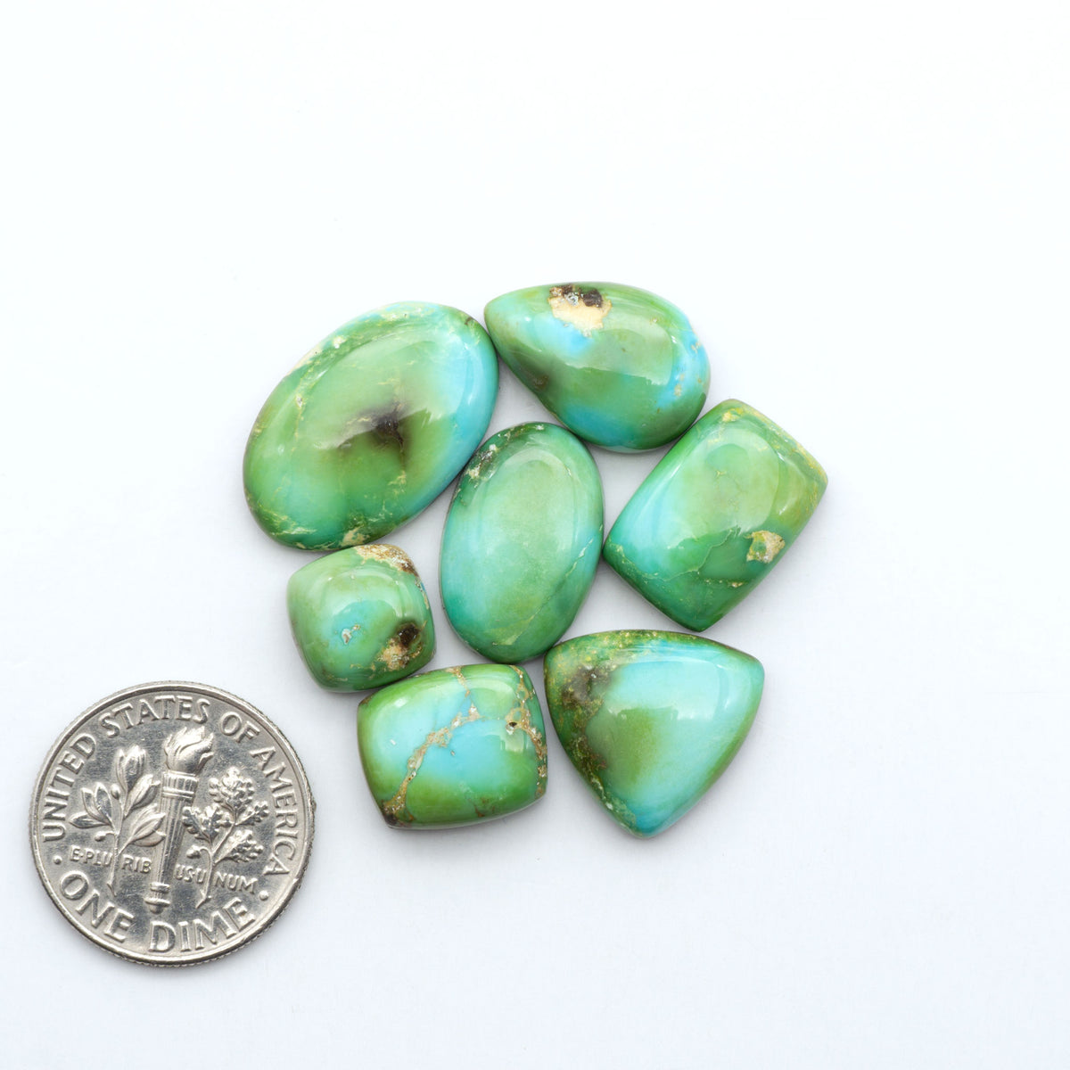 Sonoran Mountain Turquoise cabochons, blue-green color with natural matrix, polished stones on a white background, with a US dime for scale