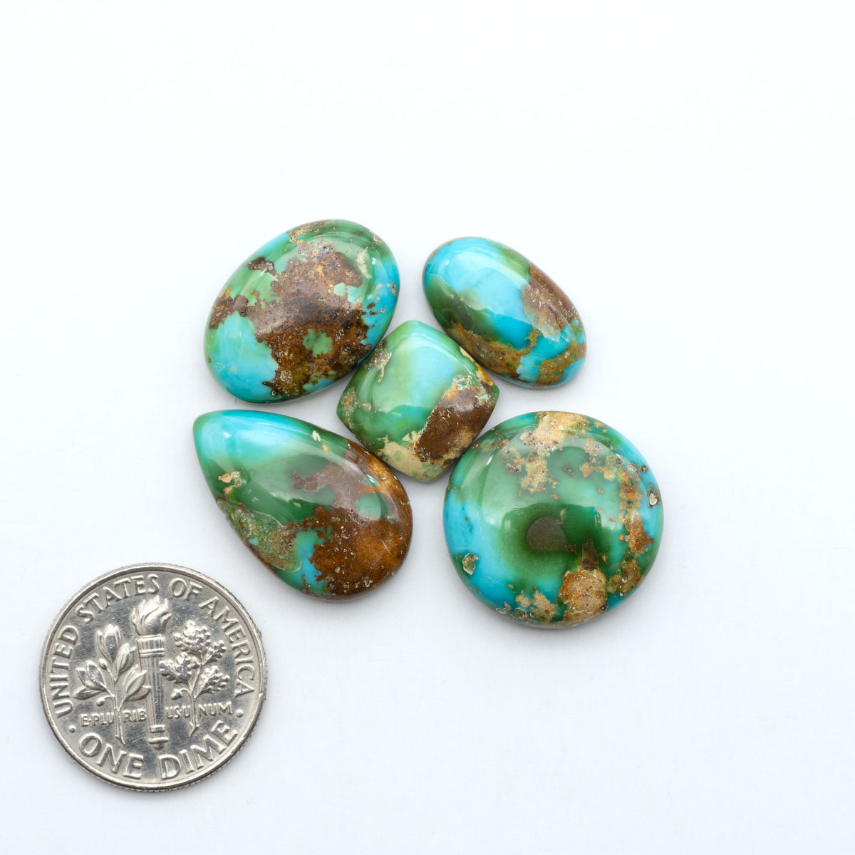 Sonoran Mountain Turquoise cabochons, blue-green color with natural matrix, polished stones on a white background, with a US dime for scale