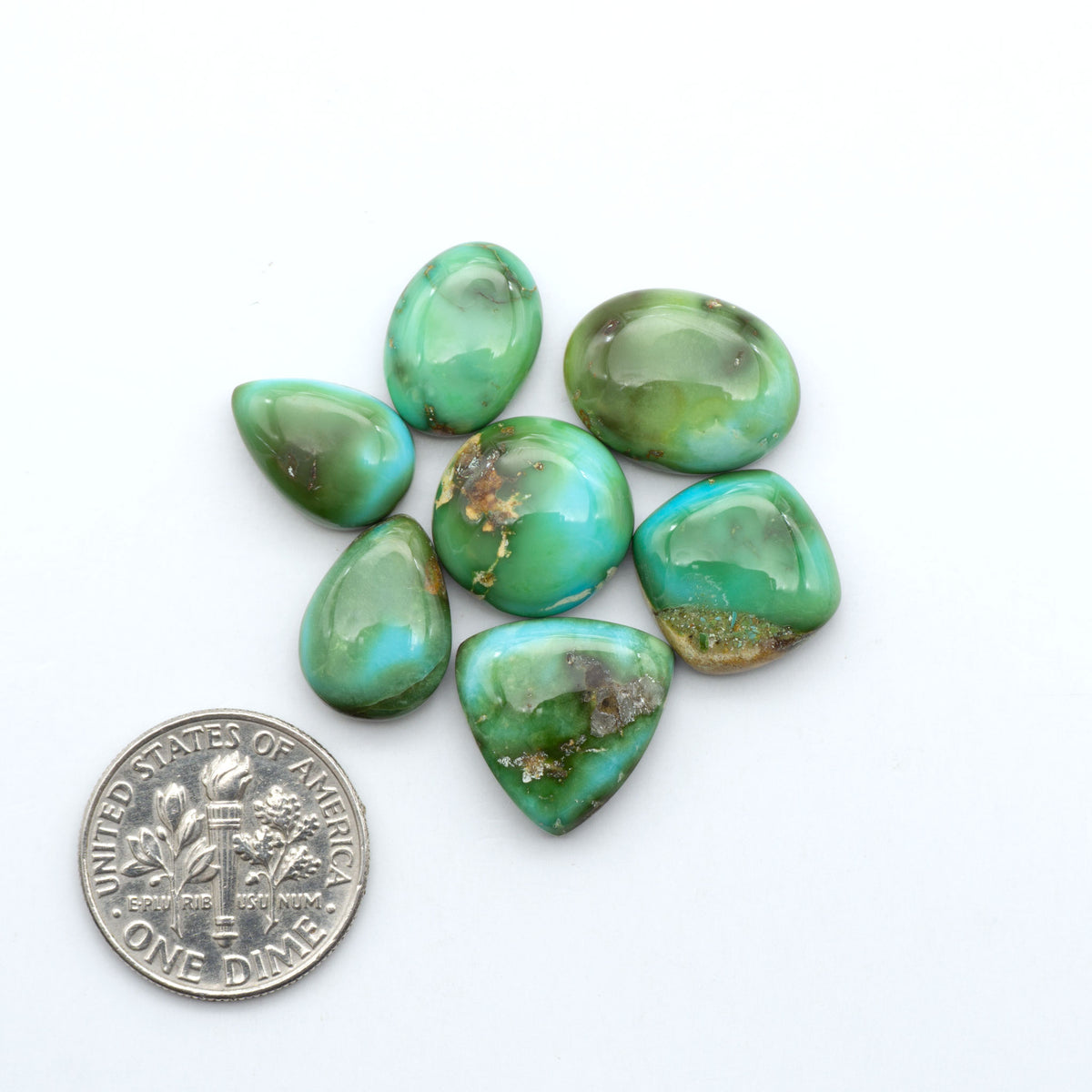 Sonoran Mountain Turquoise cabochons, blue-green color with natural matrix, polished stones on a white background, with a US dime for scale