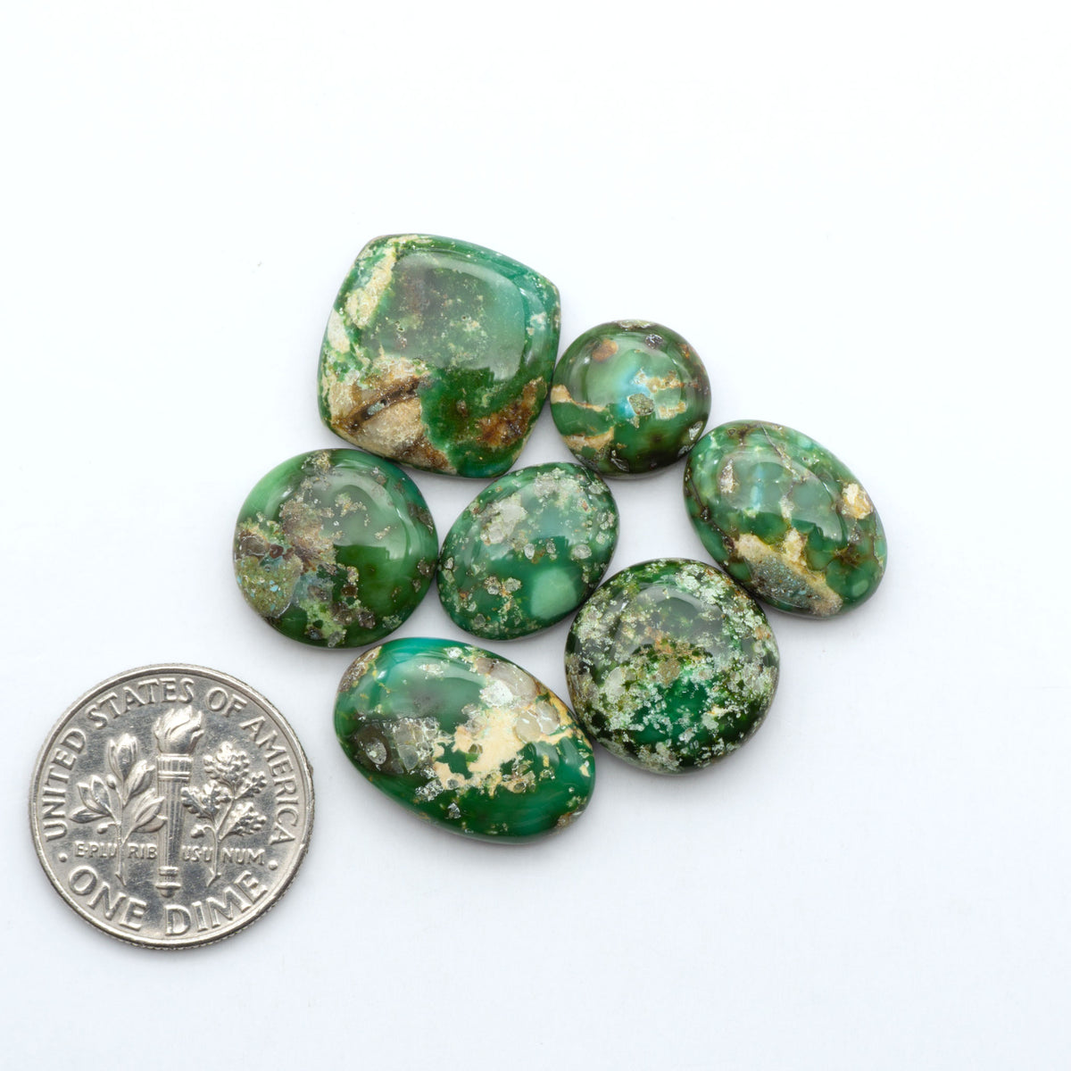 Sonoran Mountain Turquoise cabochons, blue-green color with natural matrix, polished stones on a white background, with a US dime for scale