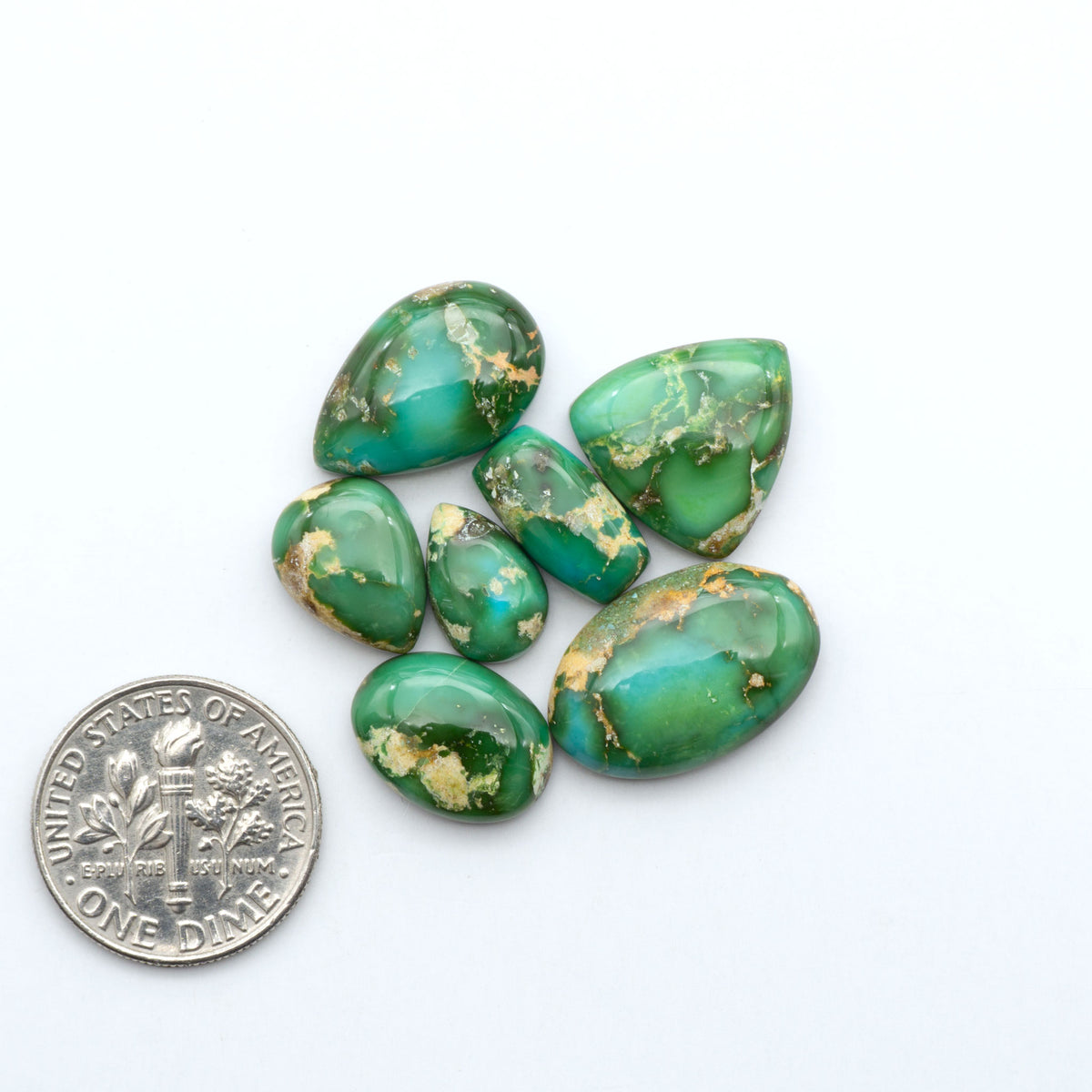 Sonoran Mountain Turquoise cabochons, blue-green color with natural matrix, polished stones on a white background, with a US dime for scale