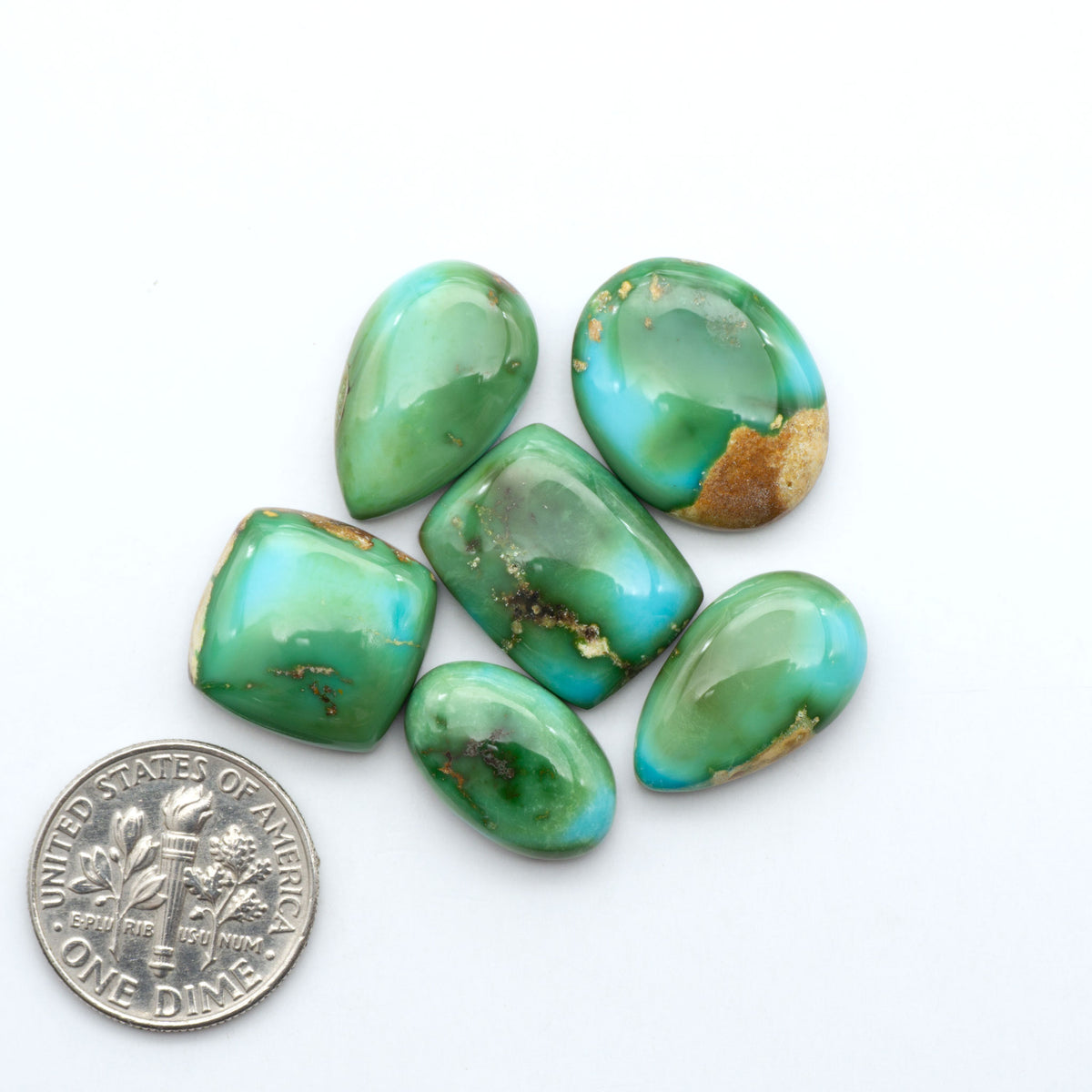 Sonoran Mountain Turquoise cabochons, blue-green color with natural matrix, polished stones on a white background, with a US dime for scale
