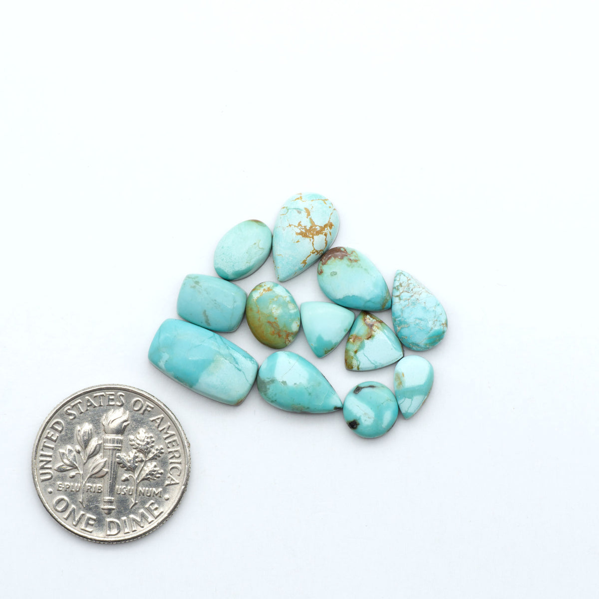 Kings Manassa Turquoise cabochons, polished green-blue gemstones with natural matrix on a white background with a US dime for scale