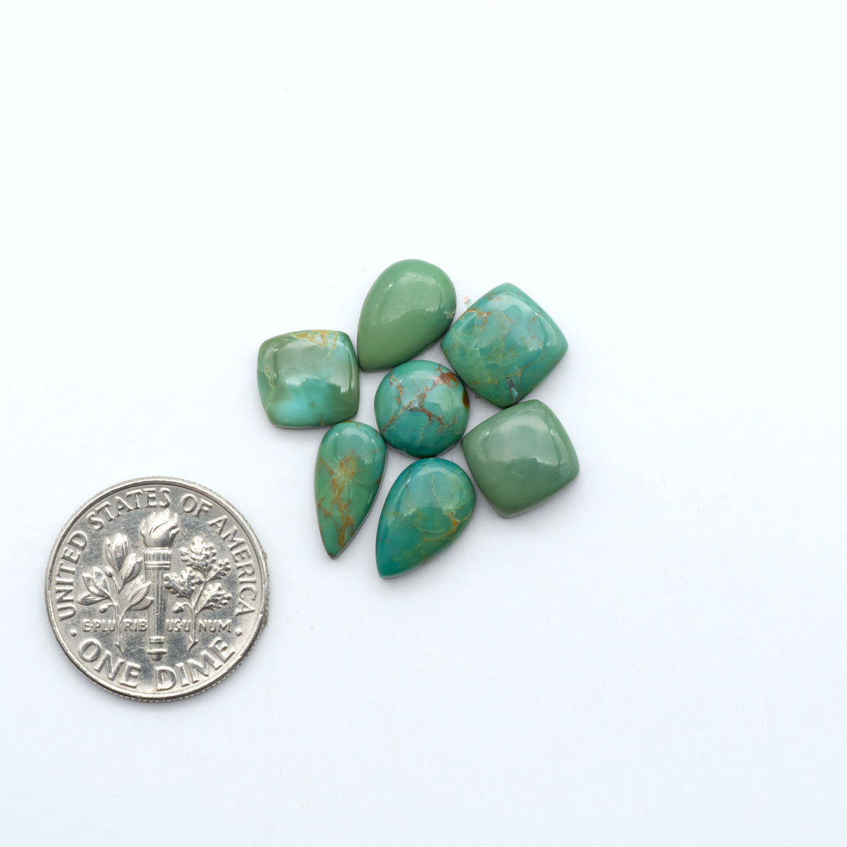 Kings Manassa Turquoise cabochons, polished green-blue gemstones with natural matrix on a white background with a US dime for scale