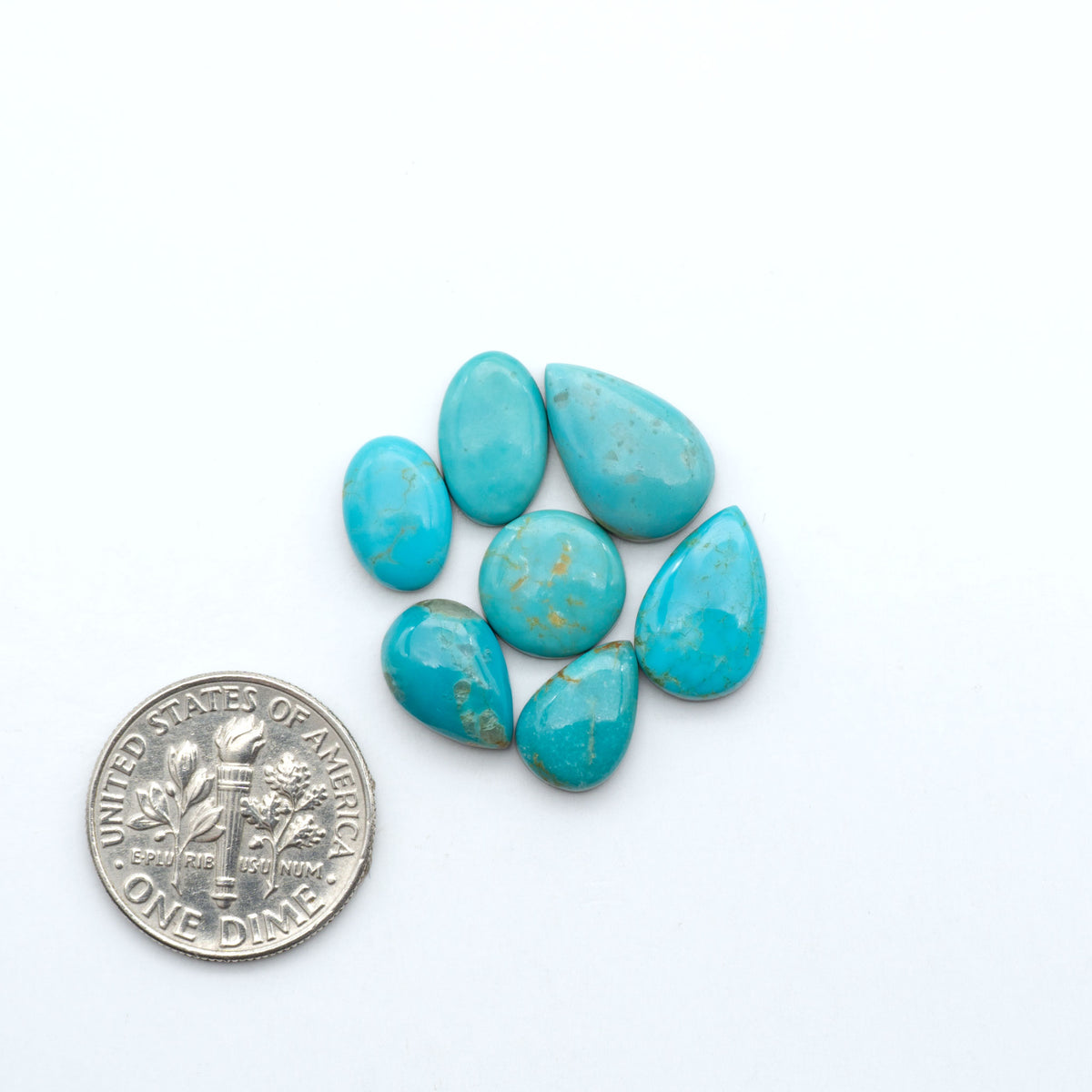 Kings Manassa Turquoise cabochons, polished green-blue gemstones with natural matrix on a white background with a US dime for scale