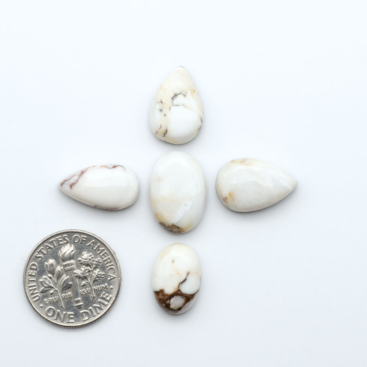 Wild Horse Magnesite cabochons, white gemstones with brown matrix on a white background, with a US dime for scale