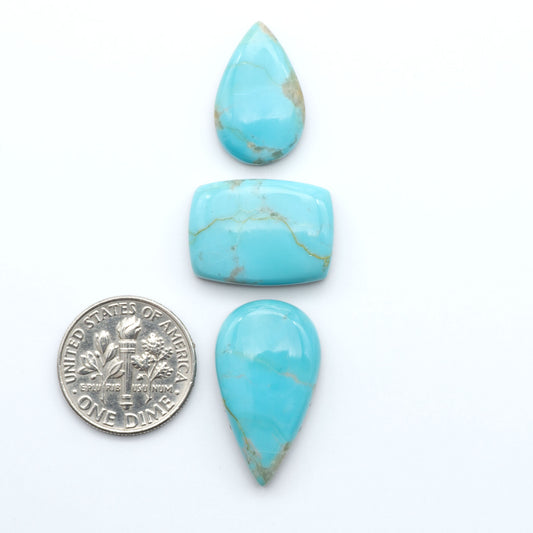 Pilot Mountain Turquoise cabochons, blue-green gemstones with natural matrix on a white background with a US dime for scale