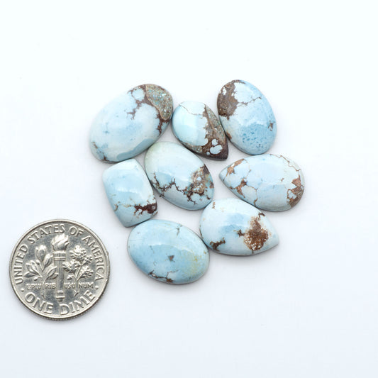 Golden Hills Turquoise cabochons, icy blue to lavender tones with chocolate matrix, polished stones on a white background with a US dime for scale