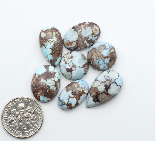Golden Hills Turquoise cabochons, icy blue to lavender tones with chocolate matrix, polished stones on a white background with a US dime for scale