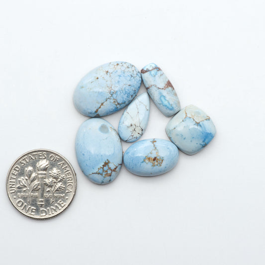 Golden Hills Turquoise cabochons, icy blue to lavender tones with chocolate matrix, polished stones on a white background with a US dime for scale
