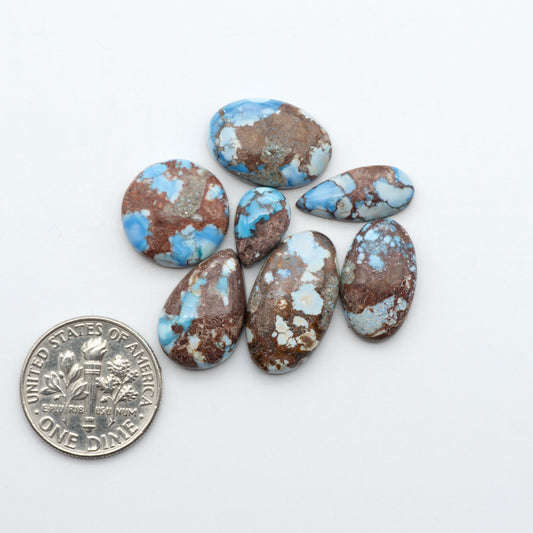 Golden Hills Turquoise cabochons, icy blue to lavender tones with chocolate matrix, polished stones on a white background with a US dime for scale