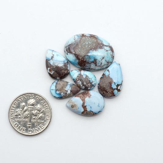 Golden Hills Turquoise cabochons, icy blue to lavender tones with chocolate matrix, polished stones on a white background with a US dime for scale