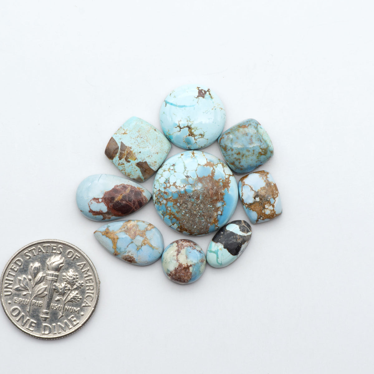 Golden Hills Turquoise cabochons, icy blue to lavender tones with chocolate matrix, polished stones on a white background with a US dime for scale