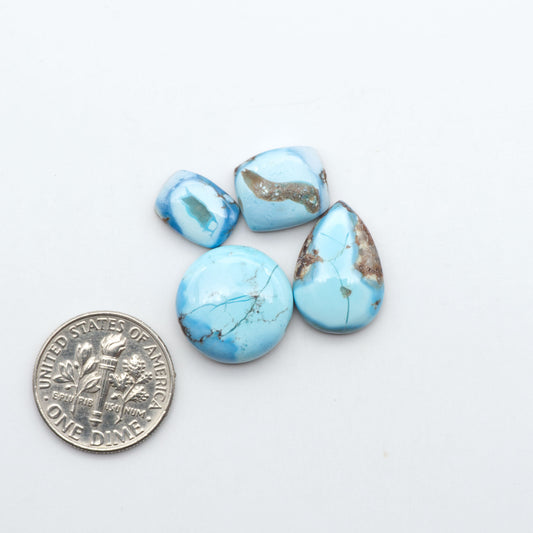 Golden Hills Turquoise cabochons, icy blue to lavender tones with chocolate matrix, polished stones on a white background with a US dime for scale