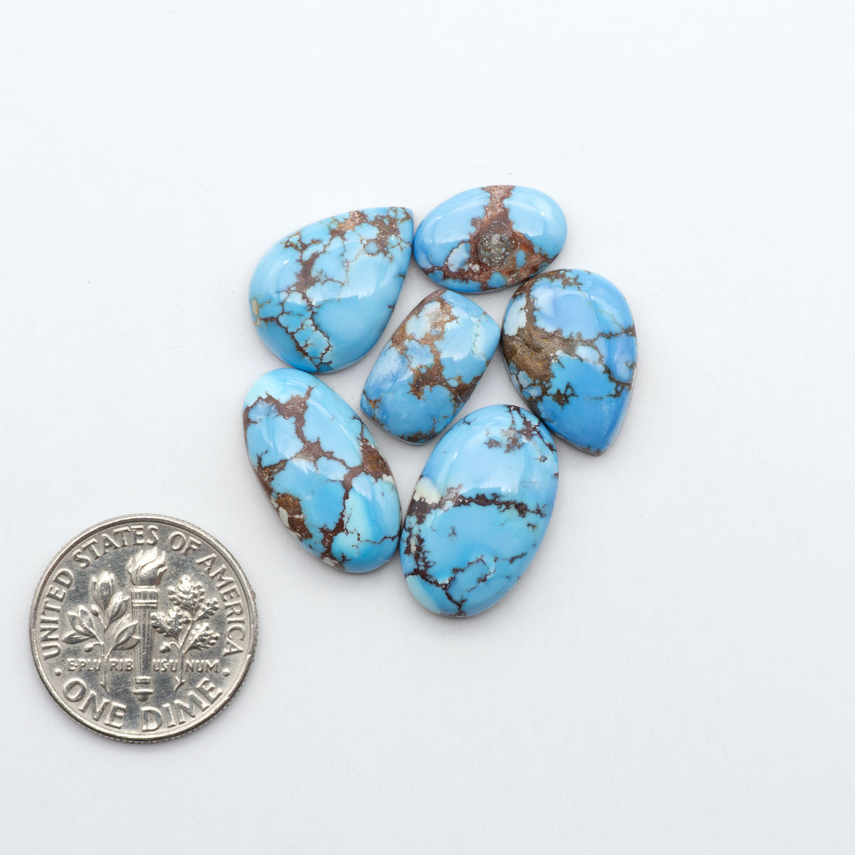 Golden Hills Turquoise cabochons, icy blue to lavender tones with chocolate matrix, polished stones on a white background with a US dime for scale