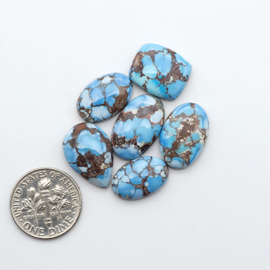 Golden Hills Turquoise cabochons, icy blue to lavender tones with chocolate matrix, polished stones on a white background with a US dime for scale