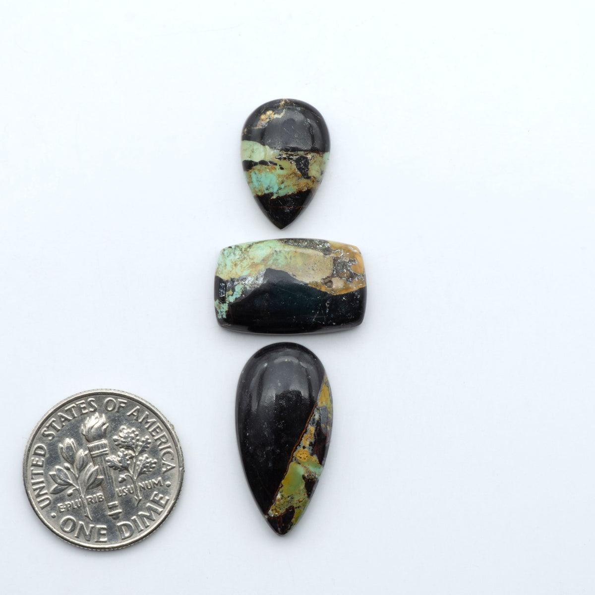 Black Jack turquoise cabochons, blue-green color with black matrix, polished stones on a white background with a US dime for scale
