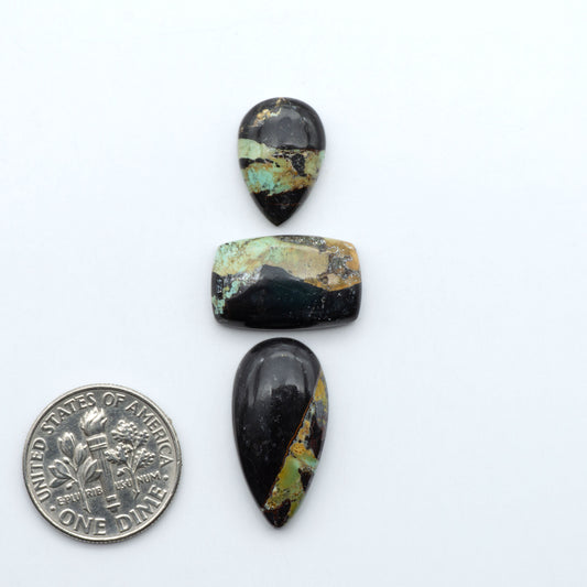 Black Jack turquoise cabochons, blue-green color with black matrix, polished stones on a white background with a US dime for scale