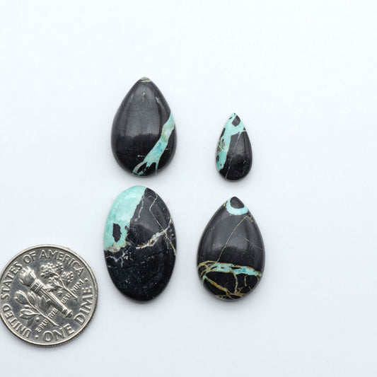 Black Jack turquoise cabochons, blue-green color with black matrix, polished stones on a white background with a US dime for scale