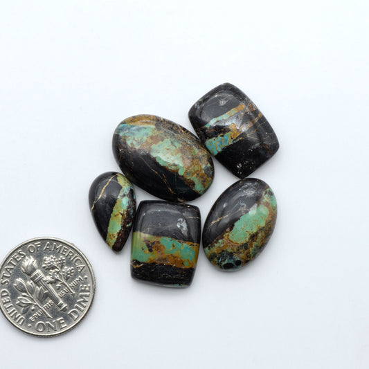 Black Jack turquoise cabochons, blue-green color with black matrix, polished stones on a white background with a US dime for scale