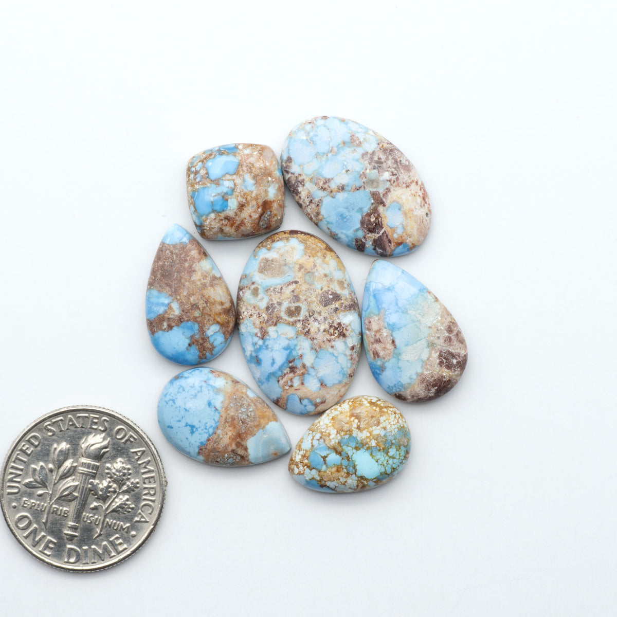Golden Hills Turquoise cabochons, icy blue to lavender tones with chocolate matrix, polished stones on a white background with a US dime for scale