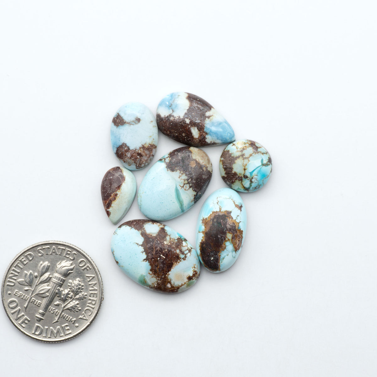Golden Hills Turquoise cabochons, icy blue to lavender tones with chocolate matrix, polished stones on a white background with a US dime for scale