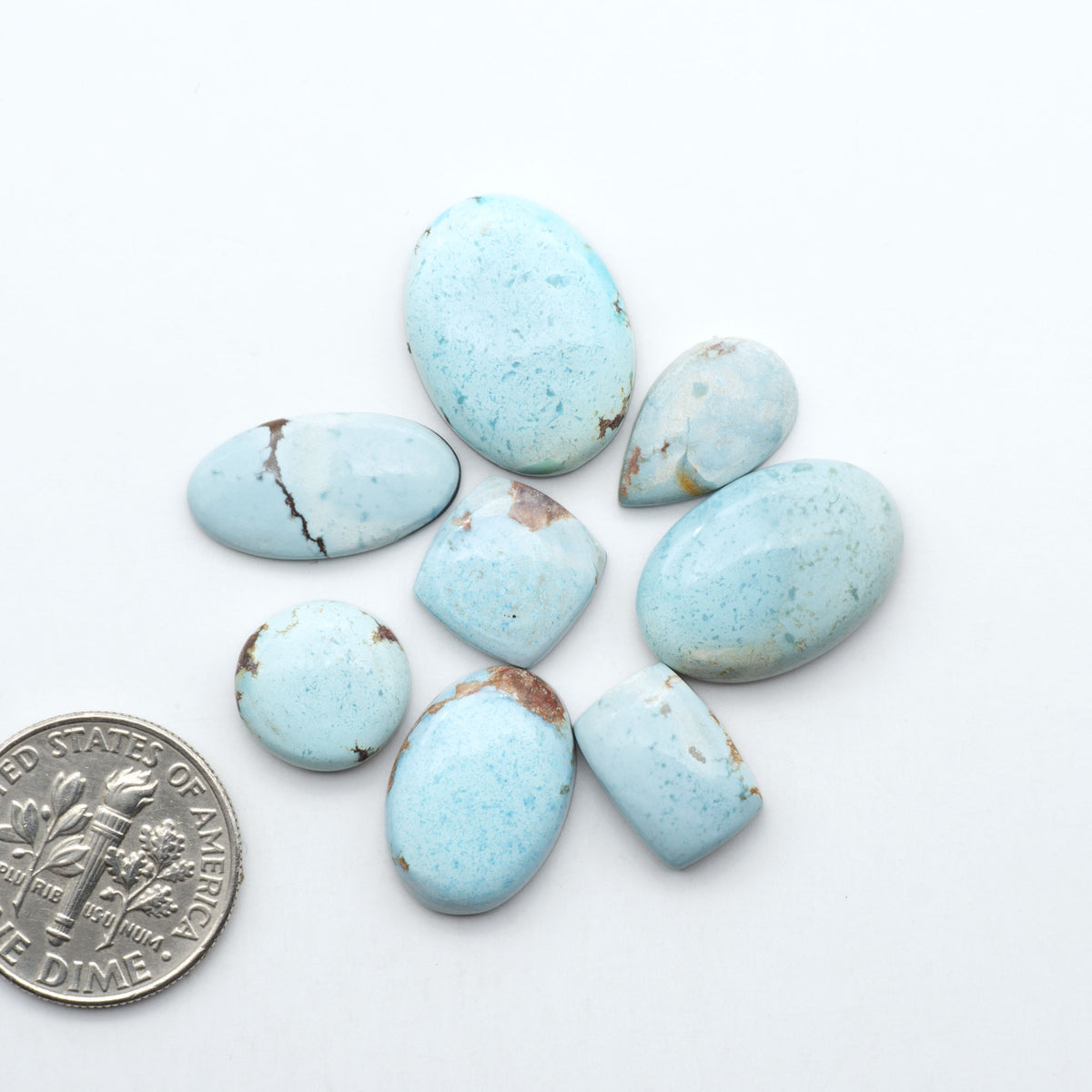 Golden Hills Turquoise cabochons, icy blue to lavender tones with chocolate matrix, polished stones on a white background with a US dime for scale