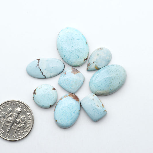 Golden Hills Turquoise cabochons, icy blue to lavender tones with chocolate matrix, polished stones on a white background with a US dime for scale