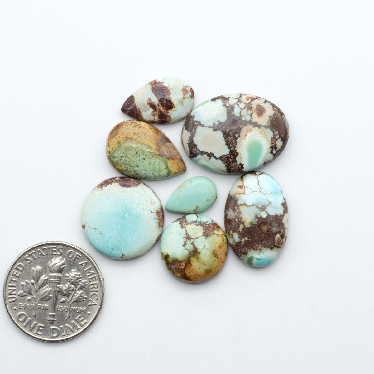 Golden Hills Turquoise cabochons, icy blue to lavender tones with chocolate matrix, polished stones on a white background with a US dime for scale